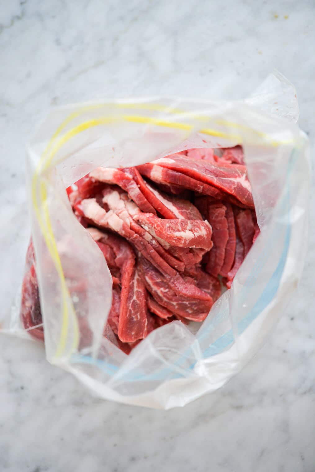 Top down view of plastic zipper bag containing raw, sliced beef