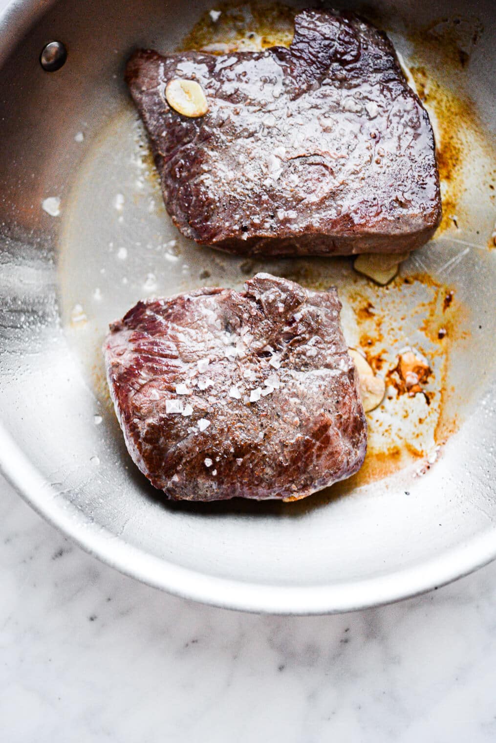 Two steaks seared in an stainless steel pan topped with flaky salt