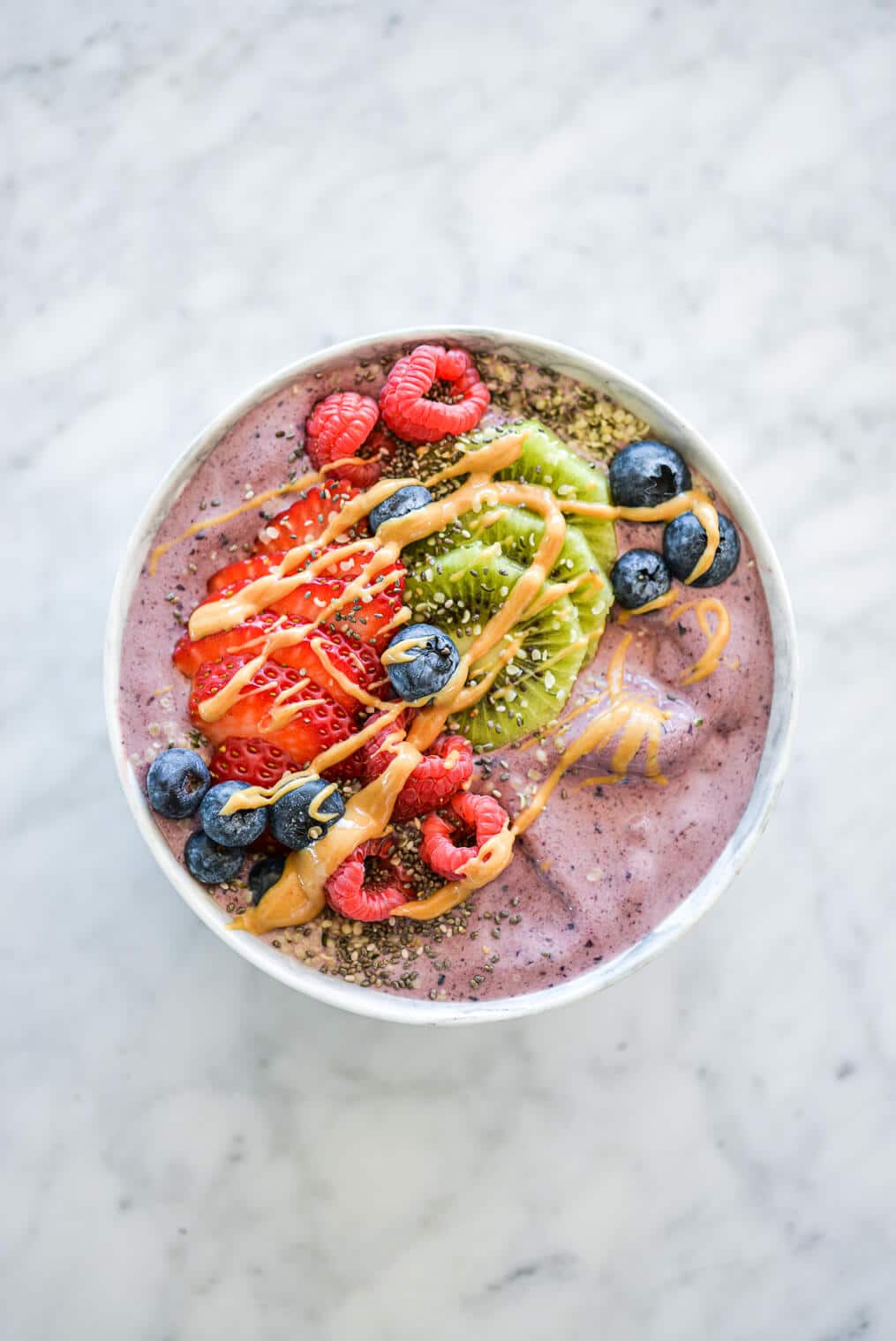 Acai smoothie bowl topped with assortment of fruit, chia seeds, and peanut butter