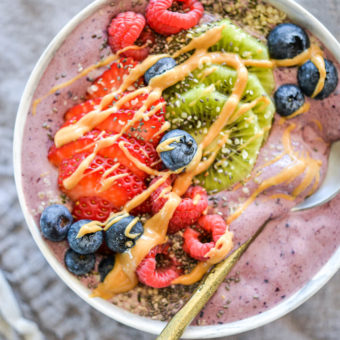 Acai smoothie bowl with spoon topped with assortment of fruit, chia seeds, and peanut butter