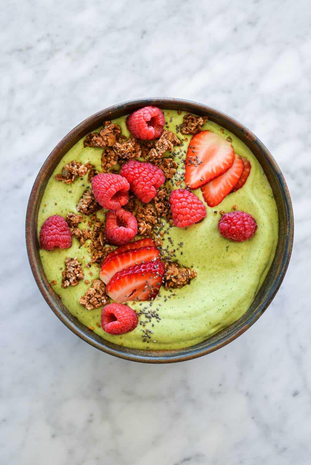 Avocado smoothie bowl topped with sliced strawberries, chia seeds, raspberries, and granola