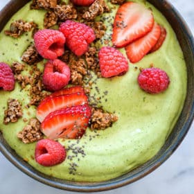 Avocado smoothie bowl topped with sliced strawberries, chia seeds, raspberries, and granola