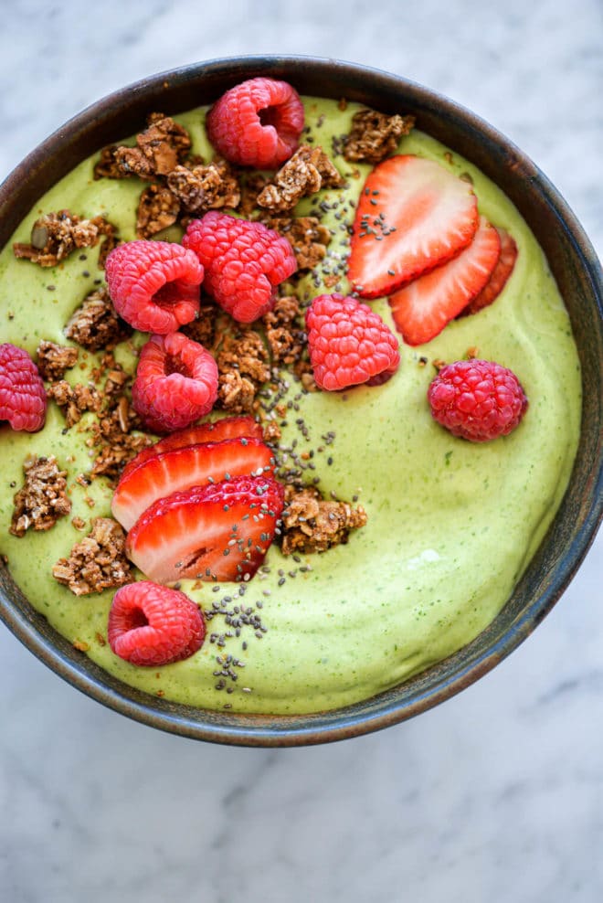 Avocado smoothie bowl topped with sliced strawberries, chia seeds, raspberries, and granola