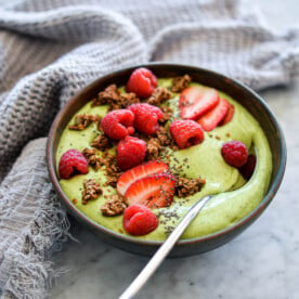 Avocado smoothie bowl topped with strawberries, raspberries, granola, chia seeds, and a spoon in a bowl.