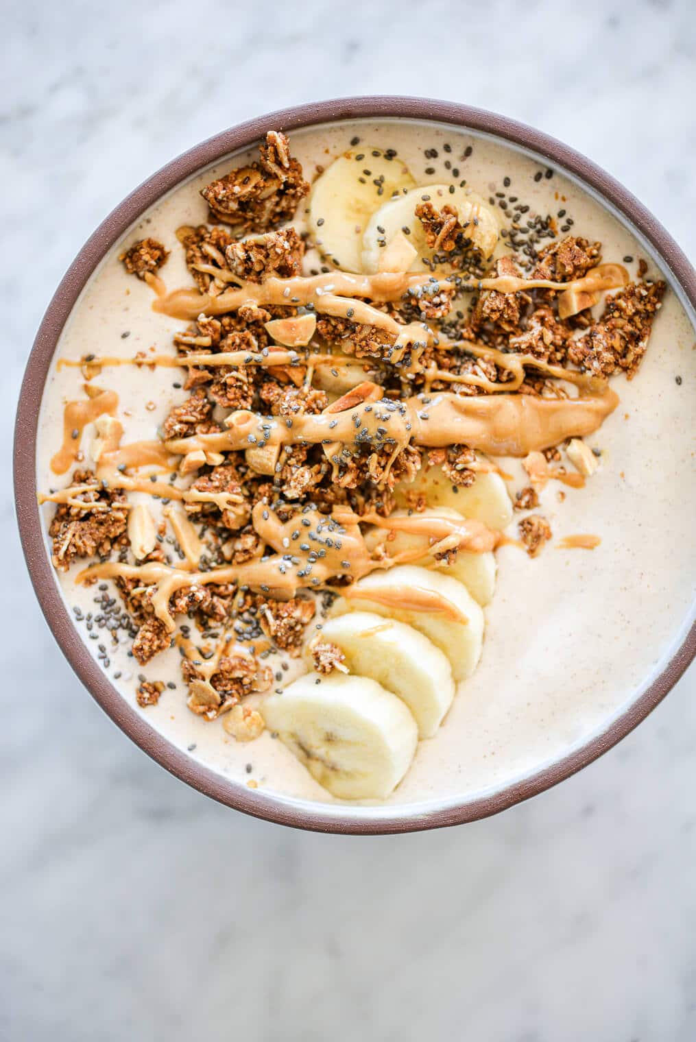 Banana smoothie bowl topped with sliced banana, granola, chia seeds, and a drizzle of peanut butter