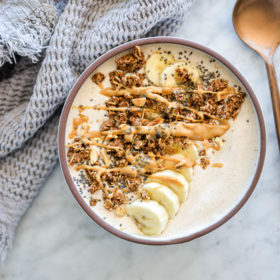 Banana smoothie bowl topped with sliced banana, granola, chia seeds, and a drizzle of peanut butter