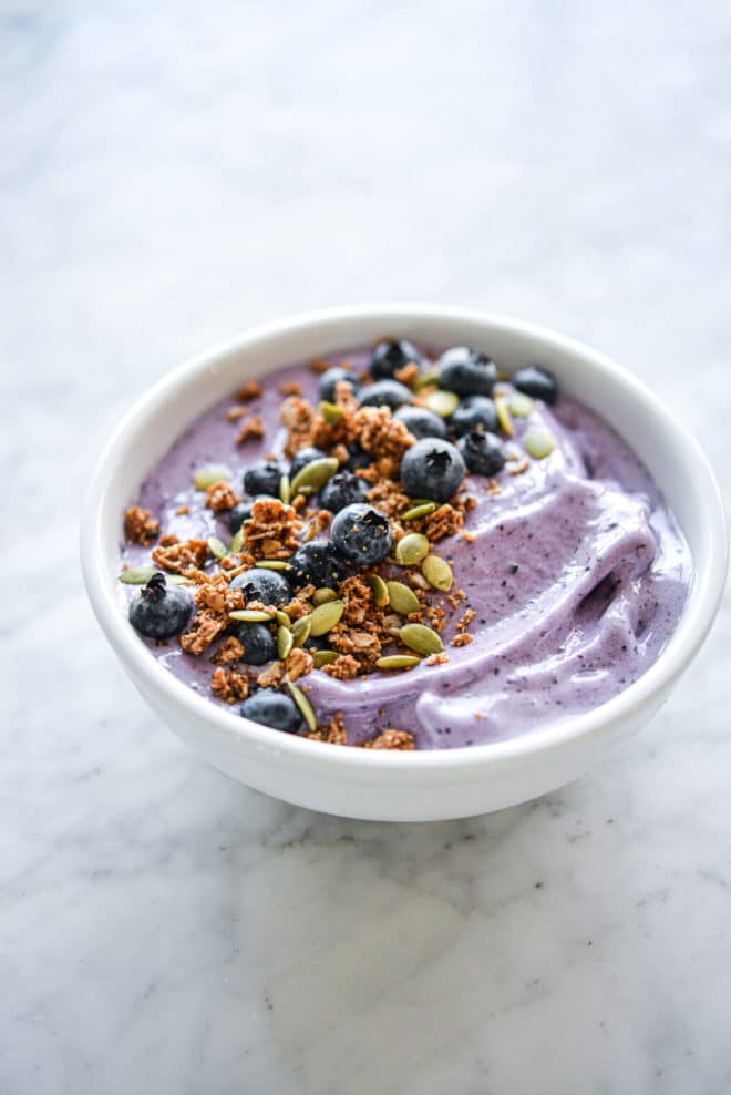 Blueberry smoothie in bowl topped with blueberries, pumpkin seeds, and granola