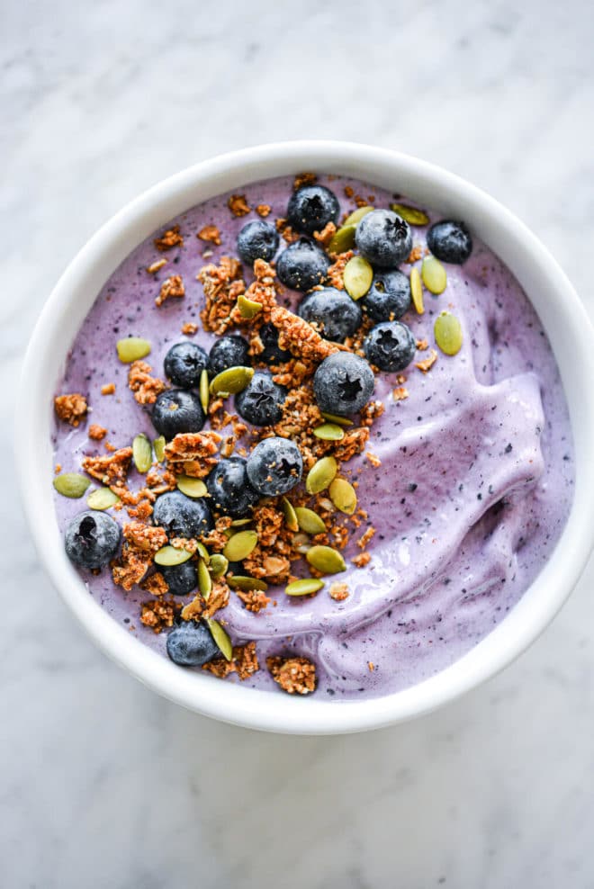 Blueberry smoothie in bowl topped with blueberries, pumpkin seeds, and granola
