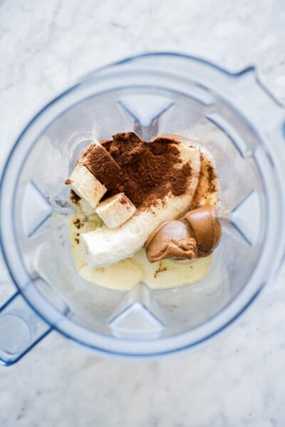 Top down view of blender with milk, cocoa powder, sliced banana, and peanut butter