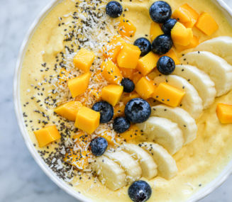 Mango smoothie in a bowl topped with sliced banana, chopped mango, blueberries, chia seeds, and coconut flakes