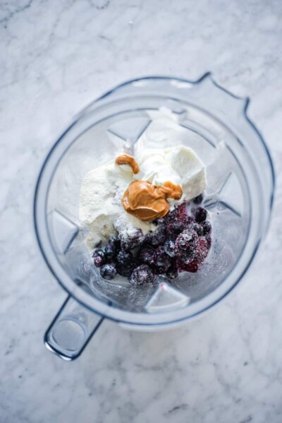 Top down view of blender with milk, protein powder, peanut butter, frozen berries, and greek yogurt