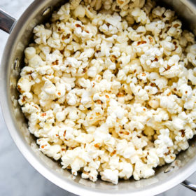 Close up of stainless steel pot with popped corn sitting on grey and white marble countertop