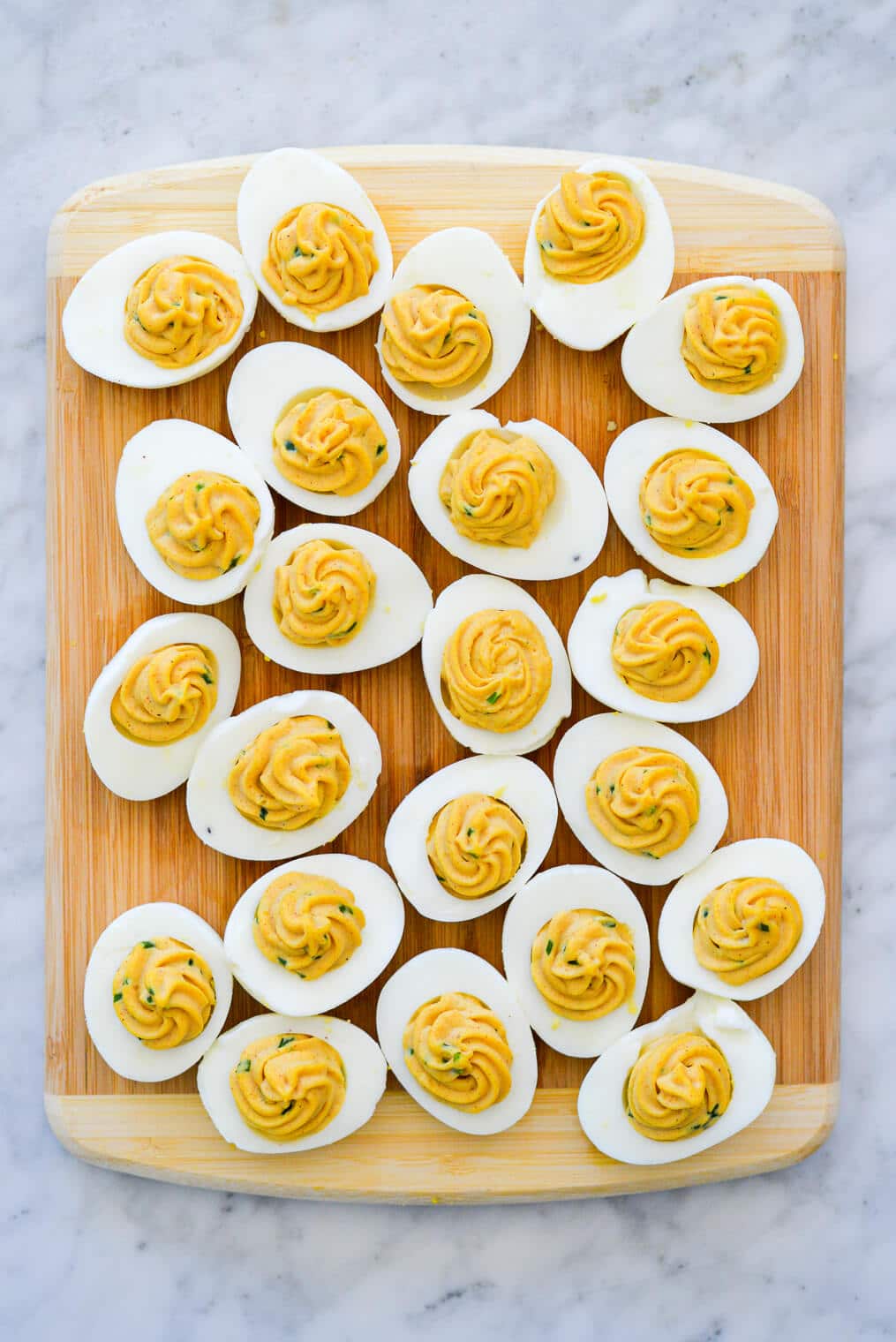 Wooden cutting board with hard boiled egg whites filled with egg yolk mixture.