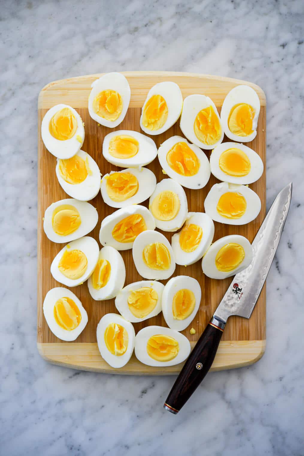 Wooden cutting board with silver knife with black handle sitting next to hard boiled eggs cut in half.