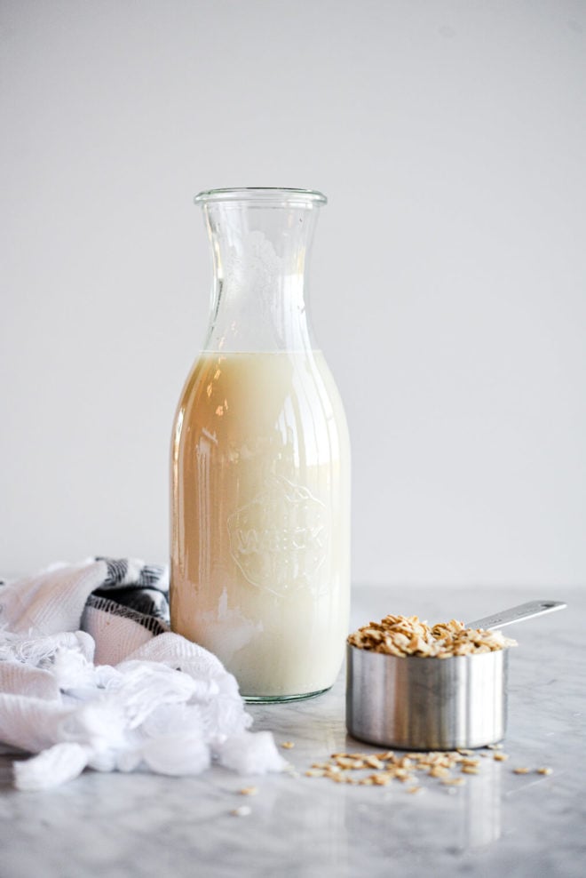 White and black kitchen towel, milk jar with oat milk, and silver measuring cup with oats.