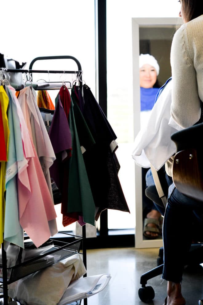 Small rolling cart with multi-colored fabric square drapes hanging around sides and blurred image of Melissa looking into a full-length mirror in the right corner.