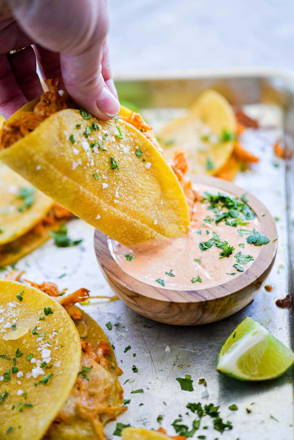 Hand holding shredded chicken taco and dipping it into creamy dipping sauce.