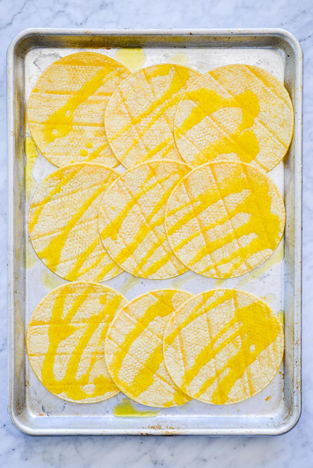 Sheet pan with three rows of three corn tortillas drizzled with olive oil.