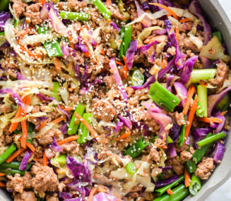 Sauté pan with egg roll in a bowl with vibrant colors of purple, orange, and green topped with sesame seeds.