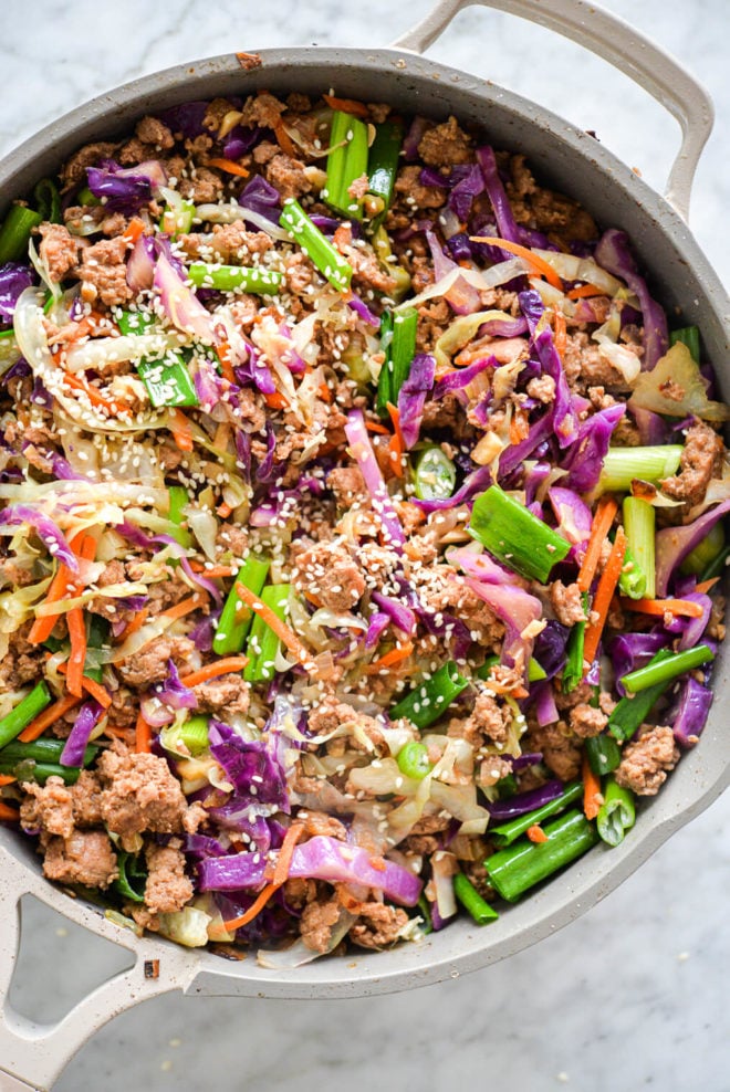 Sauté pan with egg roll in a bowl with vibrant colors of purple, orange, and green topped with sesame seeds.