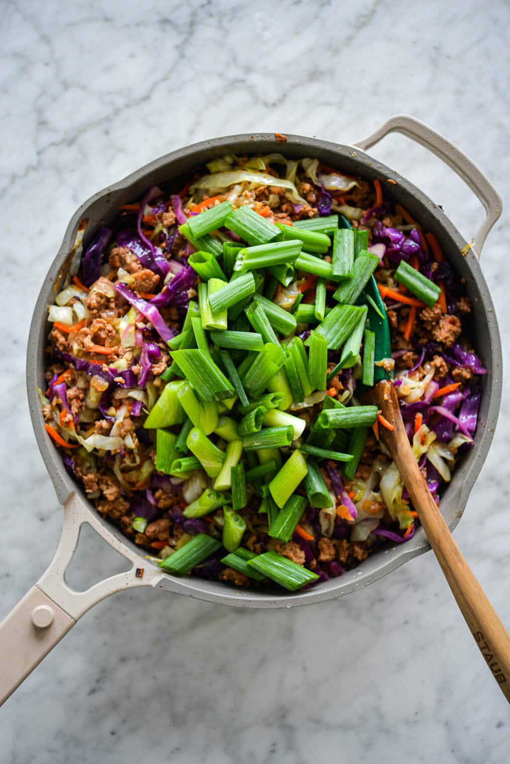 Sauté pan with egg roll in a bowl with vibrant colors of purple, orange, and green topped with sliced green onions.