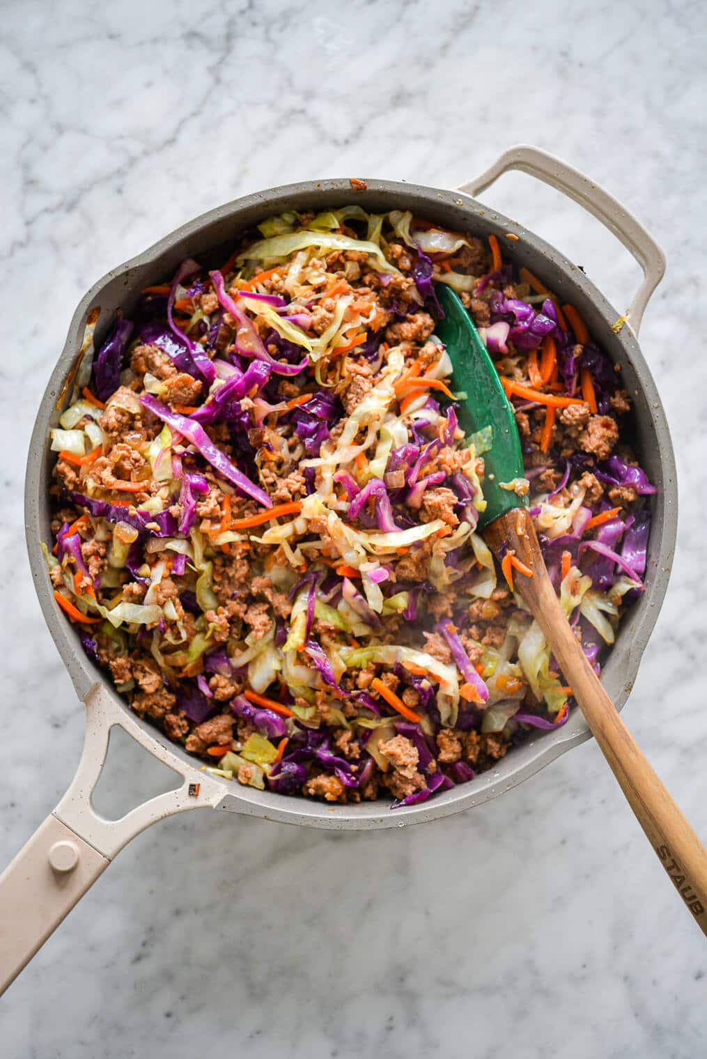 Sauté pan with egg roll in a bowl with vibrant colors of purple, orange, and green and green and brown spatula.
