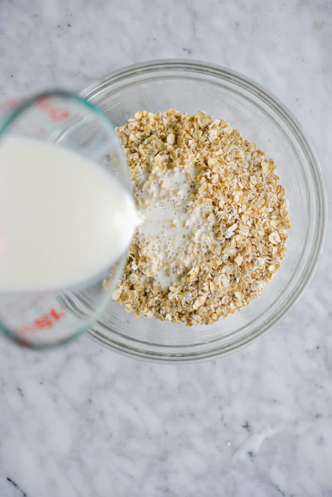 Glass bowl with dry oats and milk being poured over top.