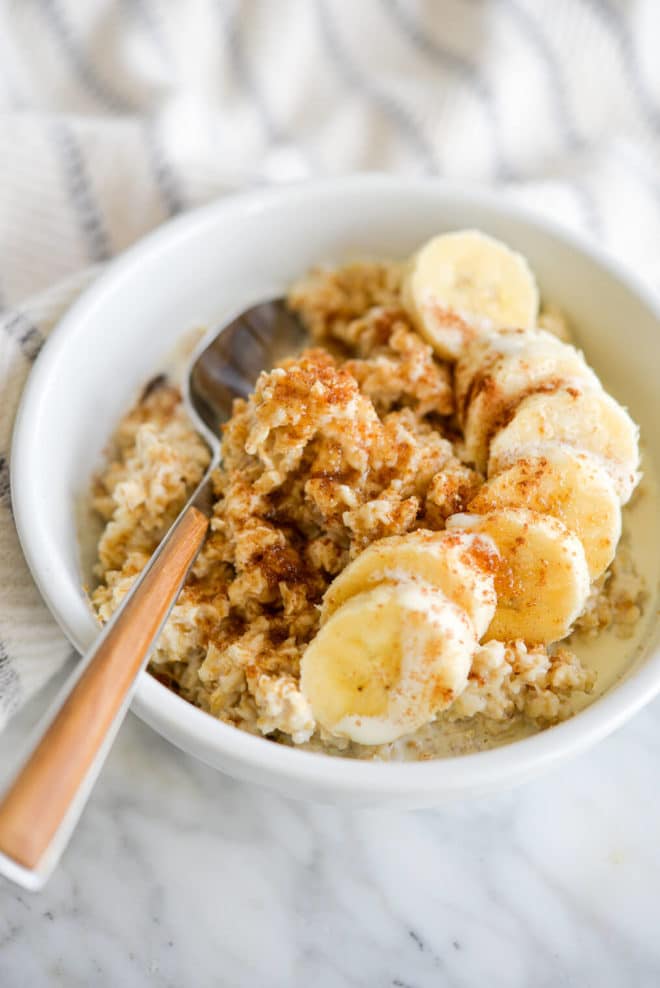 White bowl with cooked oatmeal topped with sliced banana.