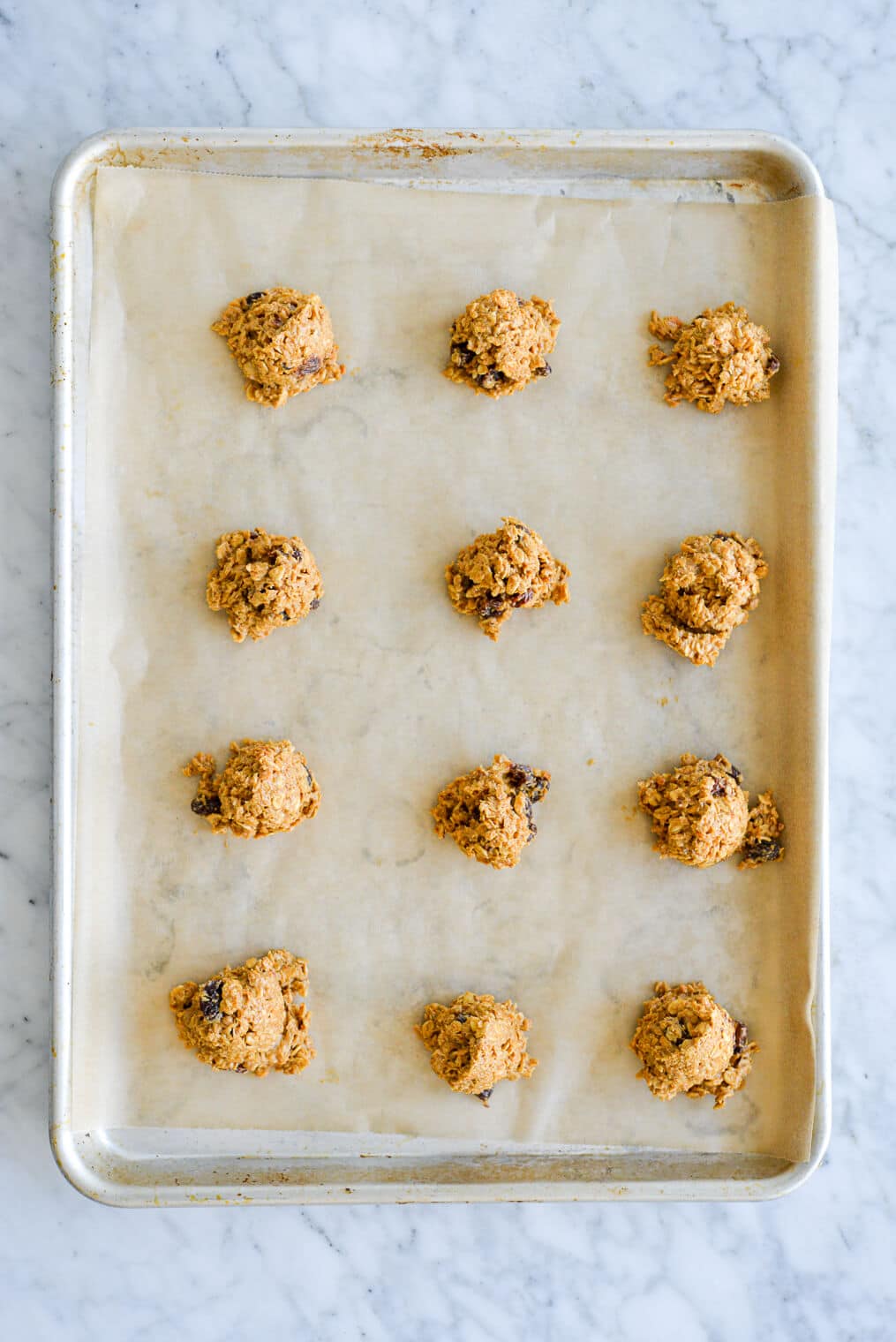 Oatmeal cookie dough scooped onto a parchment paper lined sheet pan in four rows of three.