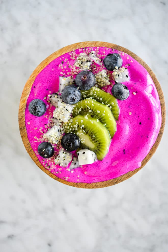 Bright magenta smoothie topped with sliced kiwi, dragonfruit, and blueberries.