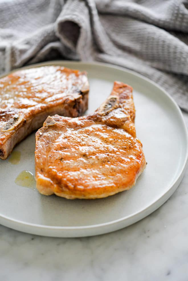 Two, juicy, bone-in cooked pork chops on a white plate.