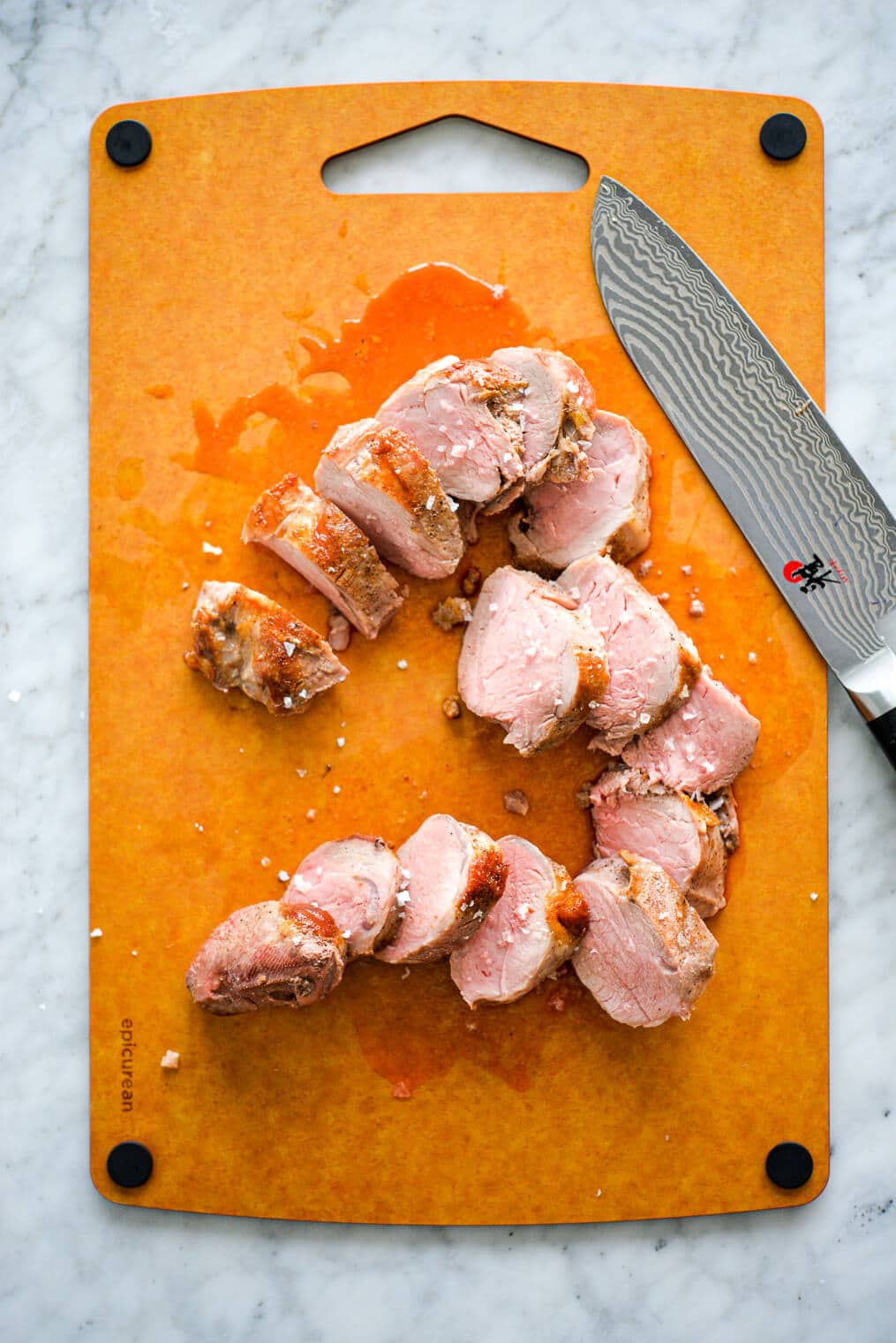Pork tenderloin slices on a cutting board with butcher knife.