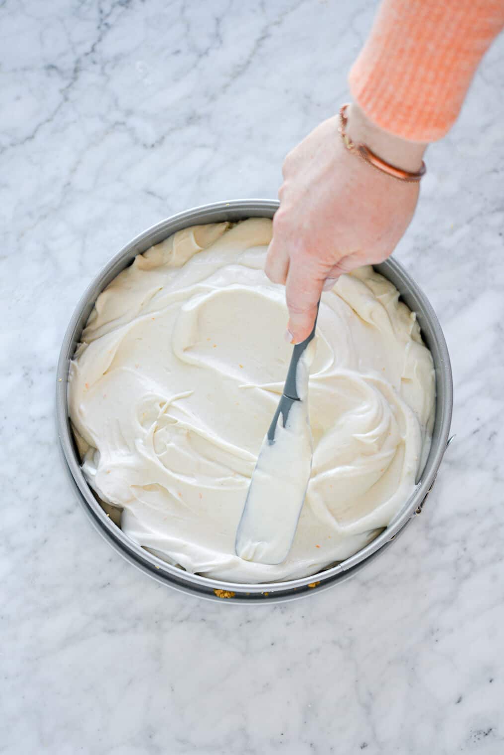 Cheesecake being spread with a spatula in a springform pan.