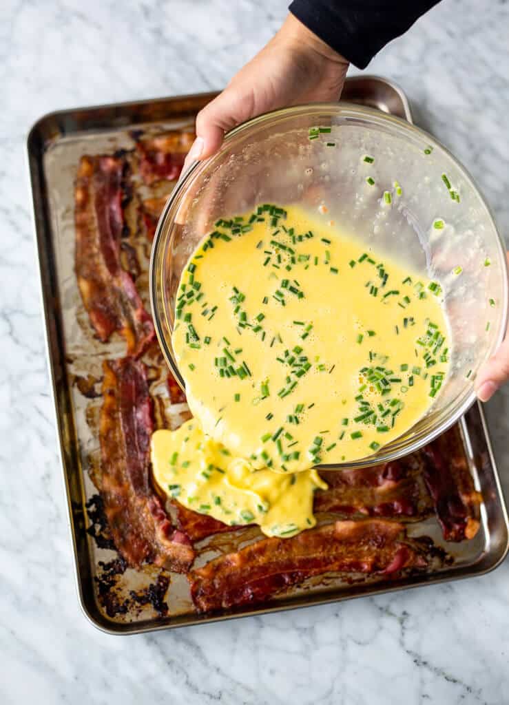 Whisked egg and chive mixture poured over bacon on a sheet pan.