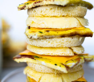 Four breakfast sandwiches stacked on top of one another on a plate.