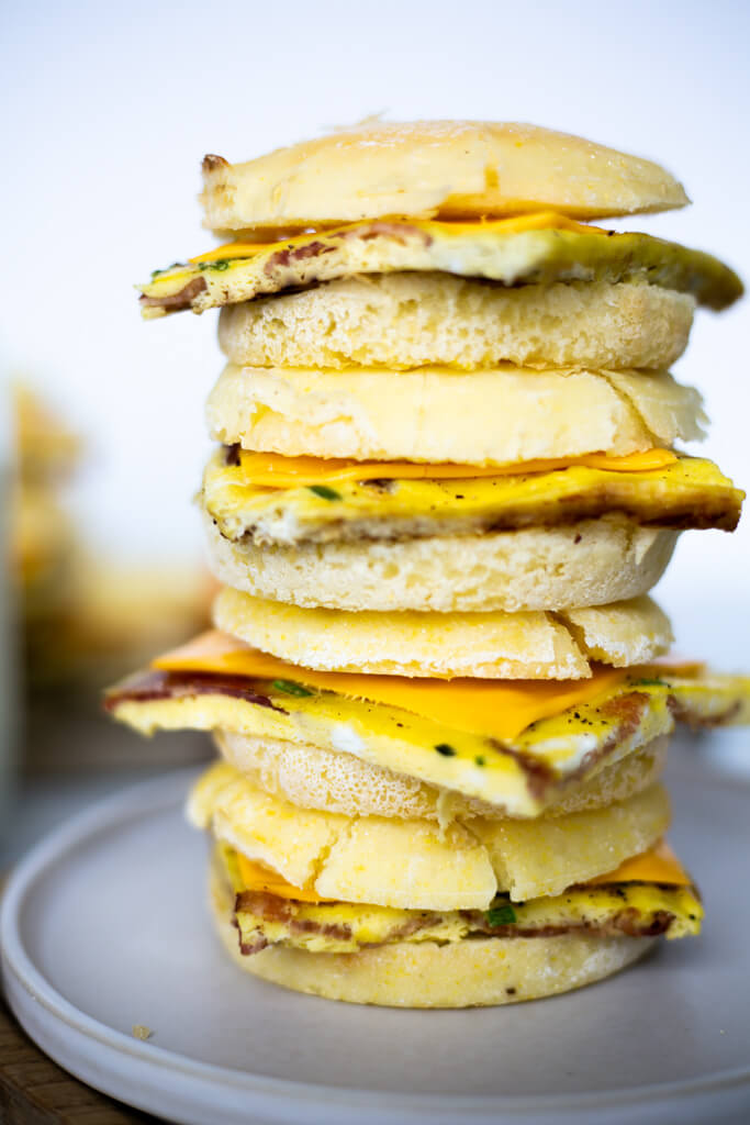 Four breakfast sandwiches stacked on top of one another on a plate.