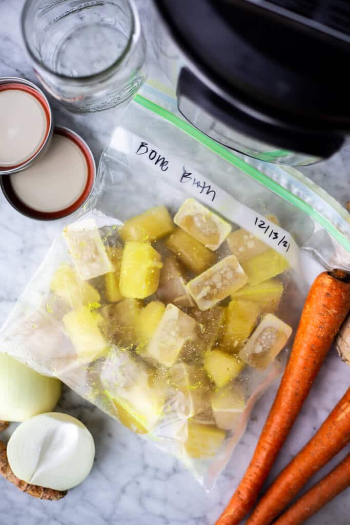 Plastic freezer bag filled with bone broth ice cubes and ingredients around the bag.