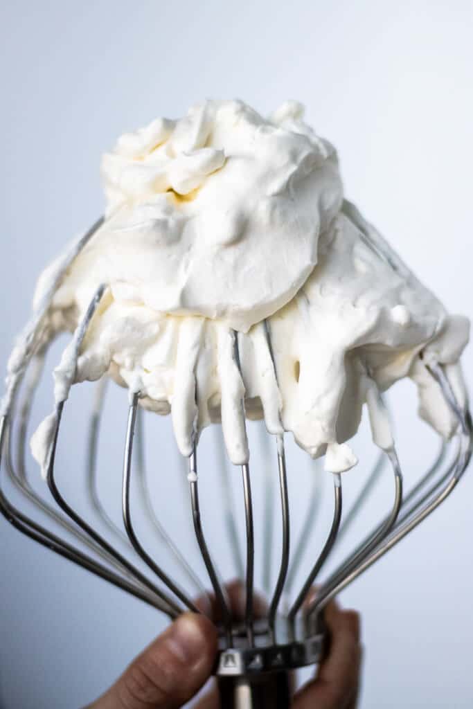 Mixer whisk being held upright with whipped cream on top.