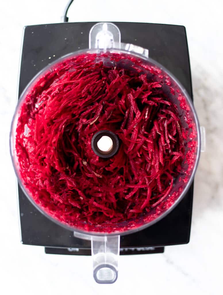 Food processor bowl with shredded beets inside.