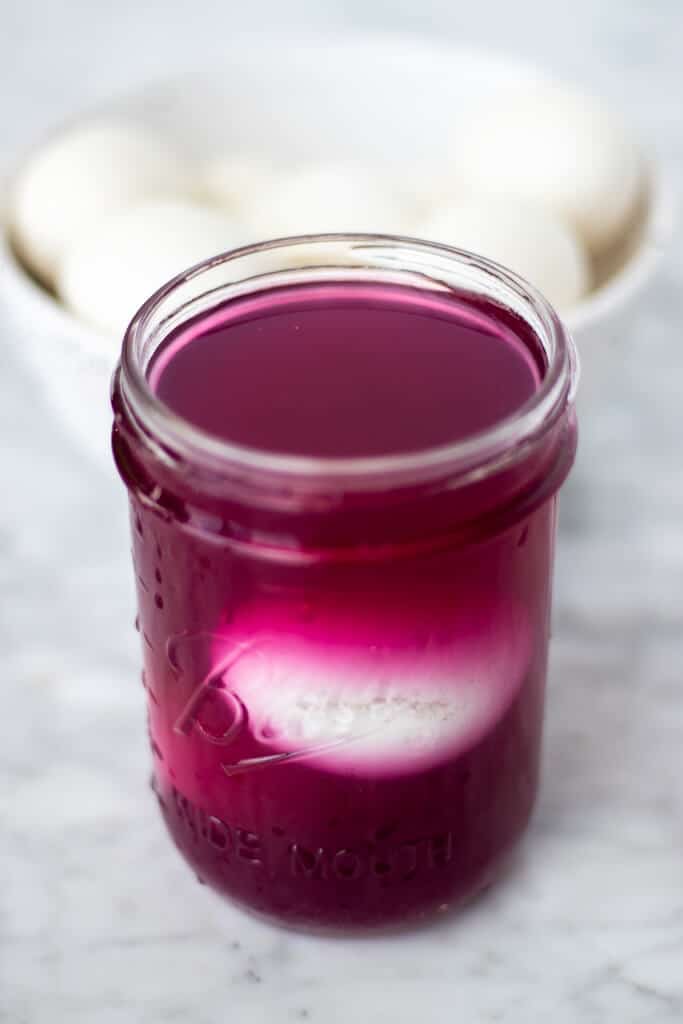 Glass mason jar with pinkish-purple colored liquid and a hard boiled egg inside.