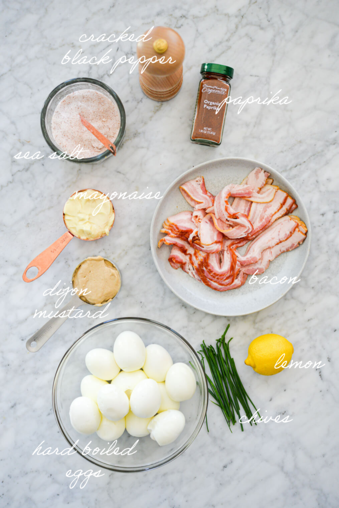 Bacon deviled egg ingredients on a marble surface with ingredient labels written in white letters.