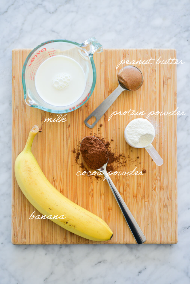 Chocolate smoothie ingredients on a wooden cutting board with ingredient labels written in white letters.