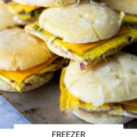 Stack of breakfast sandwiches on a sheet pan with the words "Freezer Breakfast Sandwiches" written in black underneath and "Fed + Fit" in golden orange.