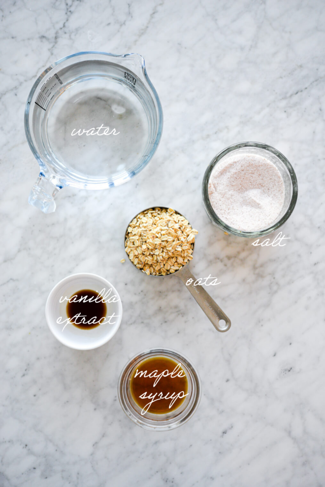 Oat milk ingredients on a marble surface with ingredient labels written in white letters.