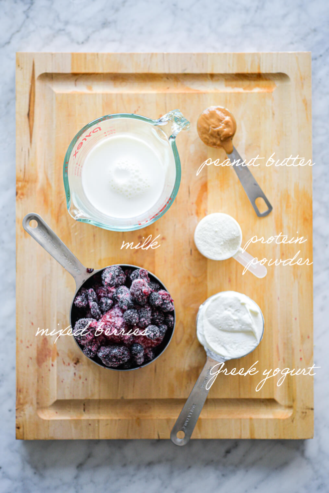 Protein smoothie bowl ingredients on a wooden cutting board with ingredient labels written in white letters.
