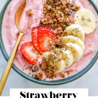 Strawberry smoothie bowl topped with sliced banana, strawberries, granola, and chia seeds with the words "Strawberry Smoothie Bowl" written in black underneath and "Fed + Fit" in golden orange.