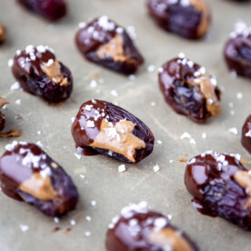 Almond butter stuffed dates dipped in chocolate with flaky sea salt on a sheet pan.