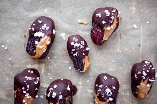 Chocolate covered, almond butter stuffed dates with flakes of sea salt on a sheet pan.