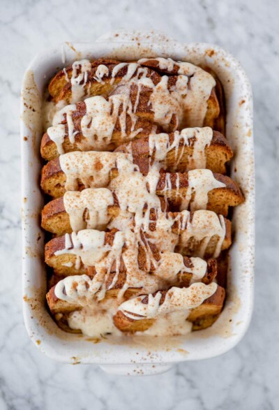 Cinnamon French toast bake drizzled with white glaze in a casserole dish sprinkled with cinnamon.