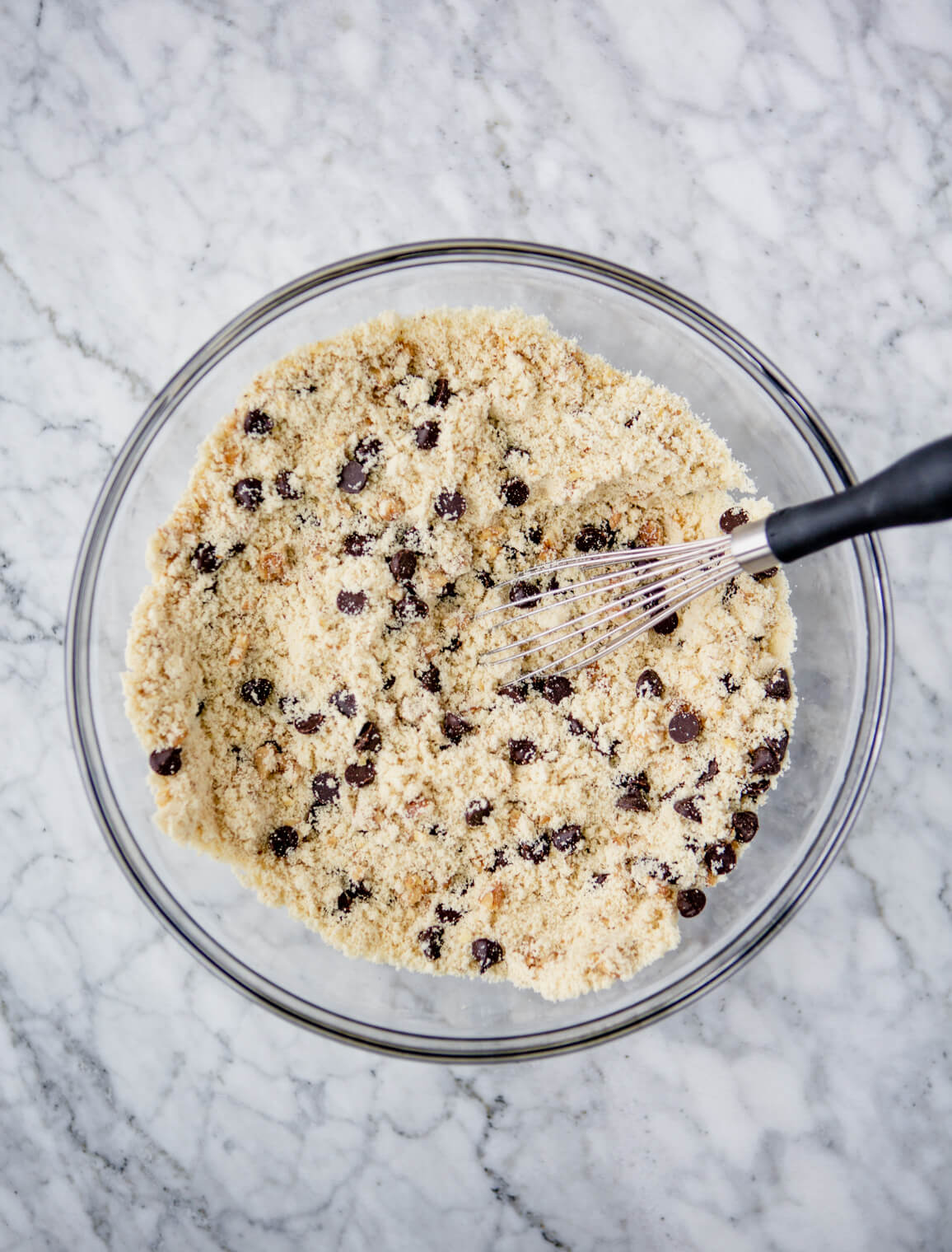 Dry ingredients combined with walnuts and chocolate chips in a bowl with a whisk.